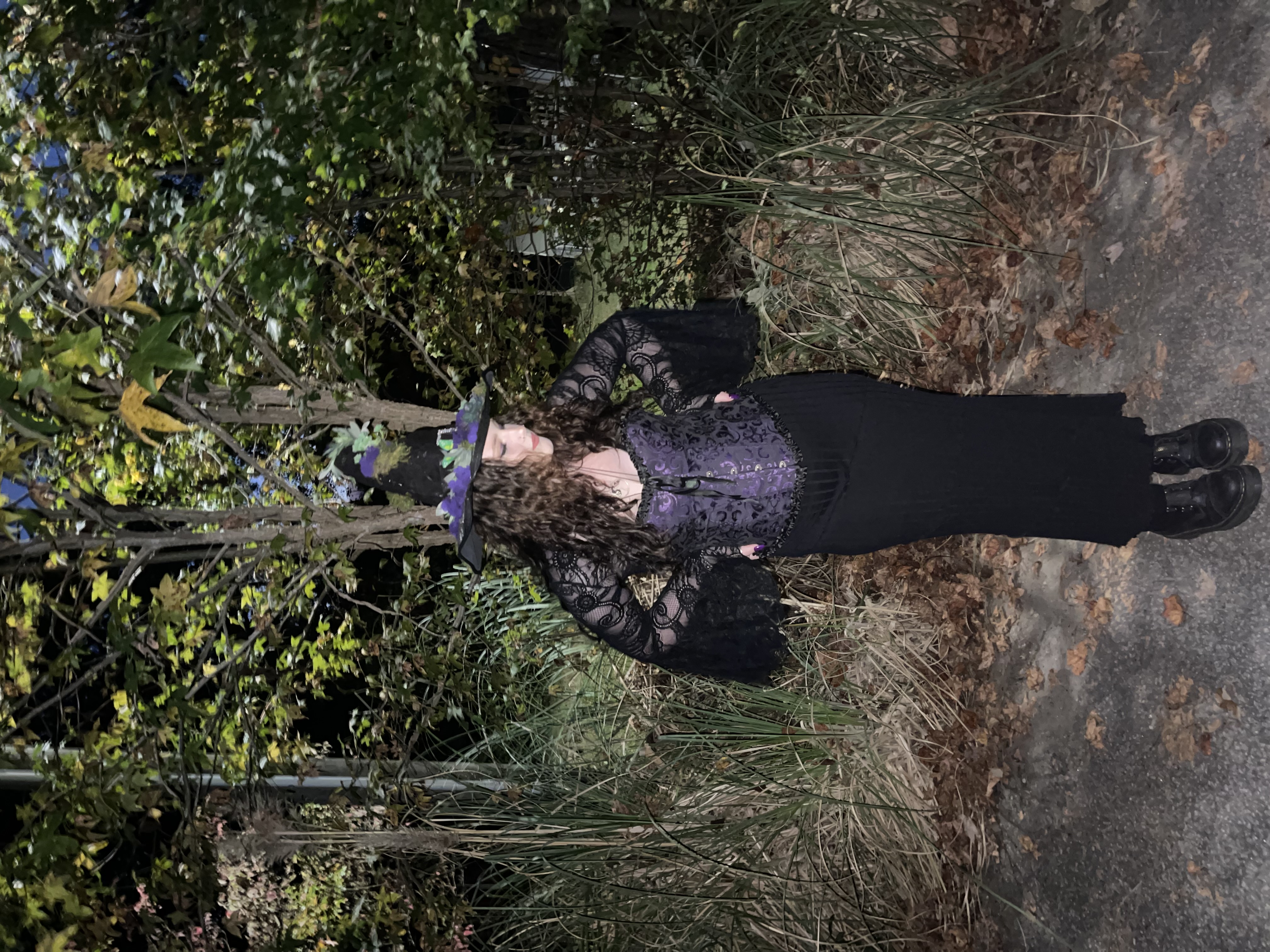 Long brown curly hair girl, wearing a witch hat, dressed in a purple corset and black skirt and lace undershirt. 